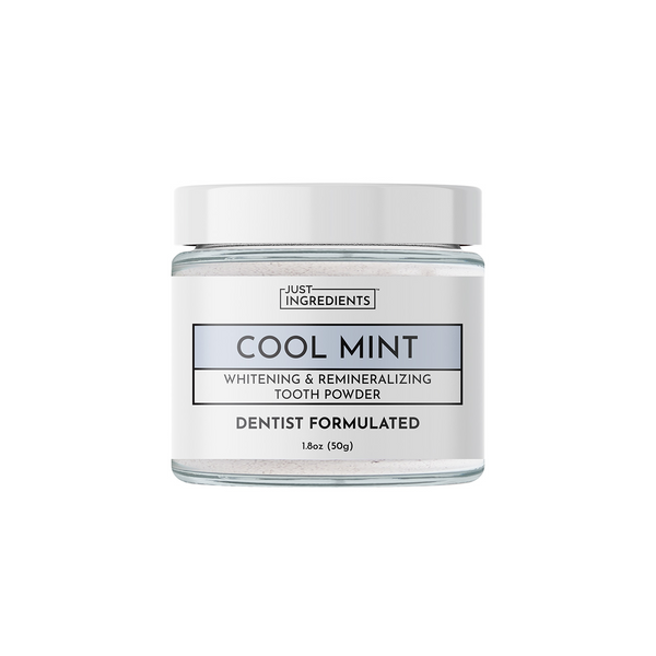 Clear glass jar of mint-flavored whitening and remineralizing tooth powder with white lid and label on a white background