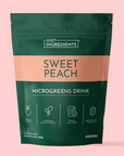 Green and peach pouch of Just Ingredients Sweet Peach Microgreens Drink with product icons and serving information on pink ba