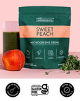 Green pouch of Sweet Peach Microgreens drink mix displayed with peach, dried microgreens, and fresh microgreen sprouts on pin