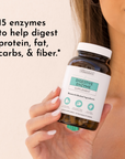 Woman holding brown glass bottle of digestive enzyme supplement with white label and white cap.