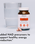 NAD+ Complex supplement bottle with white cap next to glass of water and two capsules.