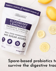 White pouch with purple accents labeled "Elderberry Lemonade Probiotic Complex" surrounded by fresh lemons on marble surface.