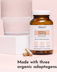 Amber glass supplement bottle labeled "Adrenal Complex" with white cap, displayed next to clear glass and two capsules on pin