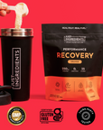 Orange-flavored recovery drink powder in black pouch with black shaker cup, shown being mixed against red background.