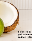 A halved coconut shell sits next to a whole lime on a light surface, with text about a potassium to sodium ratio.