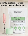 White pouch of matcha mint protein powder beside a pink milk frother and green matcha latte in a glass.