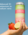 Hand holding a can of Strawberry Limeade Sparkling Electrolytes with a strawberry and lime half beside it against a blue back