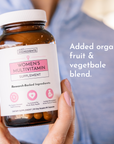Hand holding amber glass bottle of women's multivitamin supplement with white label and 90 capsules.