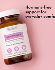 Brown glass bottle with white cap and label reading "Menopause+ Postmenopausal Support" containing 60 capsules on pink backgr
