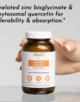 Hand holding amber glass bottle of Immune Rescue supplement with white cap and orange label.