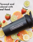 Black shaker bottle with "Just Ingredients" label surrounded by various citrus fruits and strawberries.