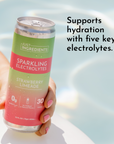A hand holds a can of Strawberry Limeade Sparkling Electrolytes by Just Ingredients near a pool.