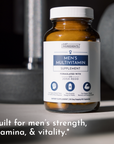 Brown bottle of men's multivitamin supplement with a white label, placed on a surface near weights.
