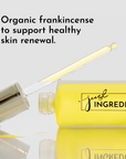 Yellow face serum bottle with dropper, labeled "just INGREDIENTS," on a reflective surface.