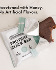 A partially unwrapped protein snack bar with a bite taken out, placed next to its packaging on a marble surface.