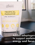 White pouch of "Tropical Paradise Pre-Workout" on a black surface, featuring yellow text and icons.