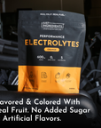 Black and orange pouch of orange-flavored electrolyte powder with nutritional information and ingredient icons visible.