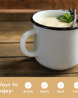 A white mug filled with creamy liquid, garnished with a mint leaf and vanilla pods, on a wooden surface.