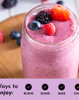 Smoothie in a glass jar topped with berries, placed on a wooden surface with scattered berries around.