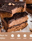Stack of chocolate-covered protein bars with a creamy center and chopped peanuts on top, placed on parchment paper.