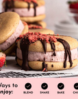 Cookies filled with strawberry cream, topped with chocolate drizzle and crushed strawberries, with fresh strawberries nearby.