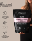 Black pouch of "Strawberries & Cream Protein Powder" held by a person, featuring product details and nutritional information.