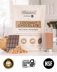Coconut Chocolate protein powder bag beside a smoothie glass and a halved coconut on countertop.