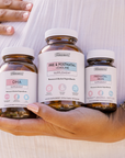 Three amber supplement bottles labeled DHA, Pre & Postnatal + Choline, and Prenatal Iron held in a hand.
