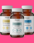 Three brown glass supplement bottles with white caps labeled Omega-3, Magnesium Complex, and Methylated B Complex on pink bac