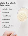 Cream-colored protein powder in a glass bowl with a hand holding a scoop below.
