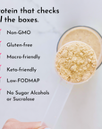 Tan protein powder in a measuring scoop with a mixed caramel latte shake in a glass behind it.