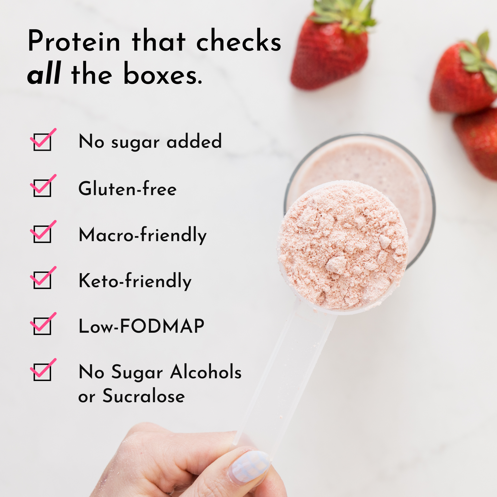 A hand holds a clear scoop of pink protein powder above a glass with a smoothie and fresh strawberries in the background.