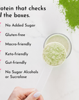 Green powder in glass with scoop held in hand, showing fine texture.