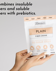 A person holds a white and peach package labeled "Plain Fiber Drink" with nutritional information and claims.