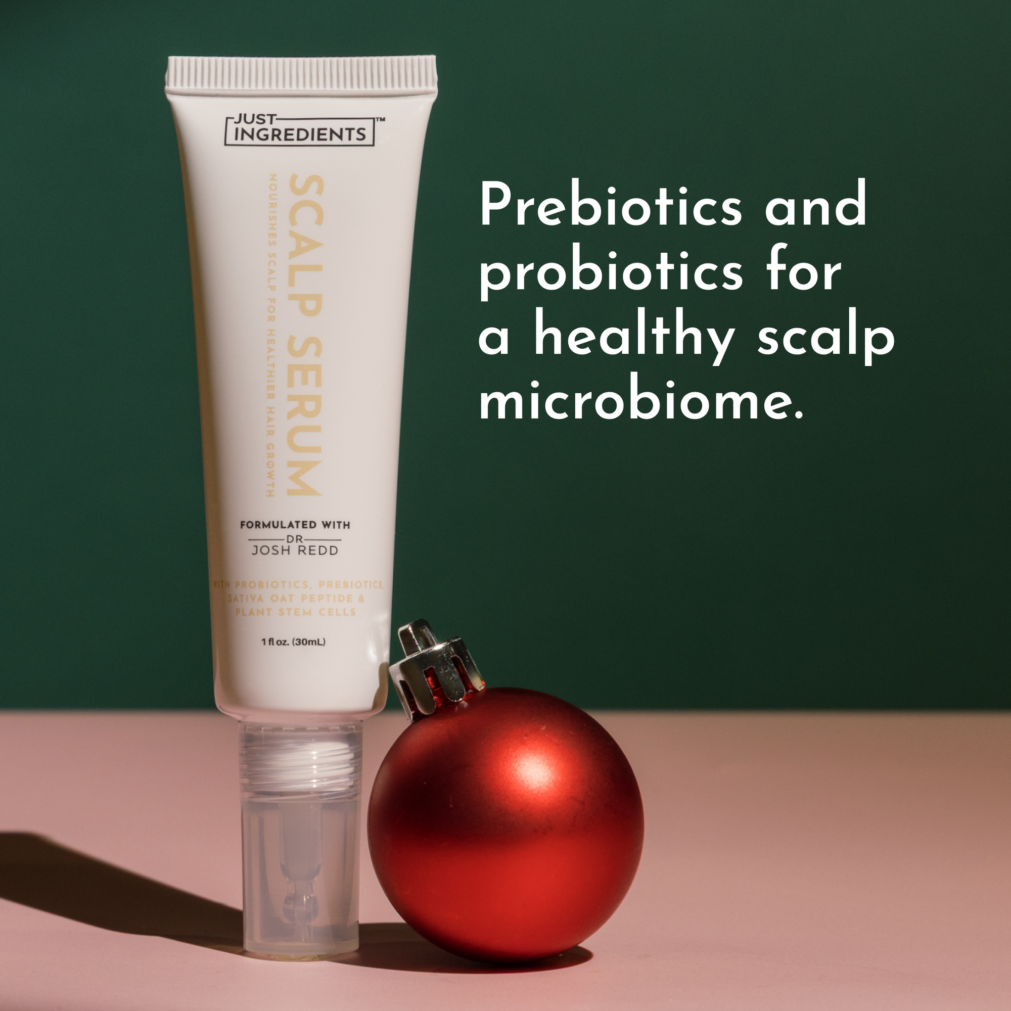 Scalp serum tube with a pump, placed next to a red ornament on a pink surface and green background.