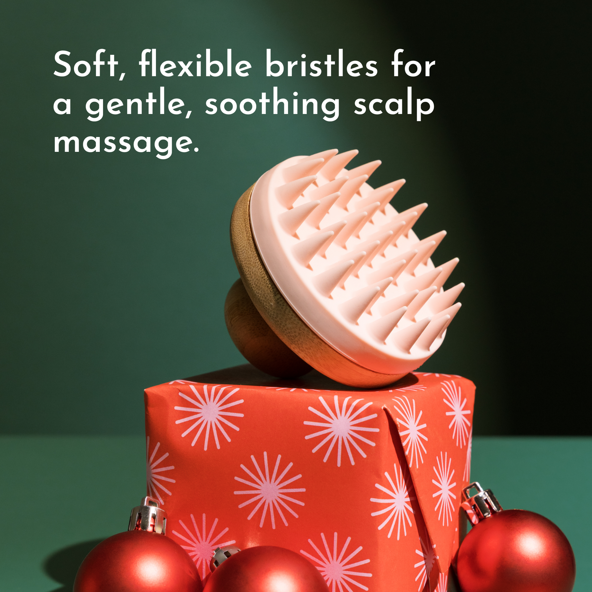 Scalp scrubber with soft, flexible bristles resting on a decorated gift box with red ornaments.