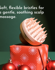 Scalp scrubber with soft, flexible bristles resting on a decorated gift box with red ornaments.