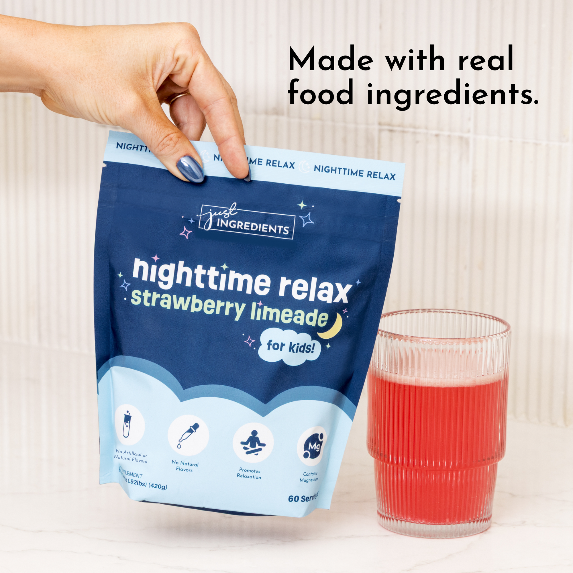Blue pouch of strawberry limeade powder held in hand next to a glass of prepared red beverage.