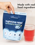 Blue pouch of strawberry limeade powder held in hand next to a glass of prepared red beverage.