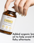 Hand holding amber glass bottle of Omega-3 DHA+EPA supplement with white label.