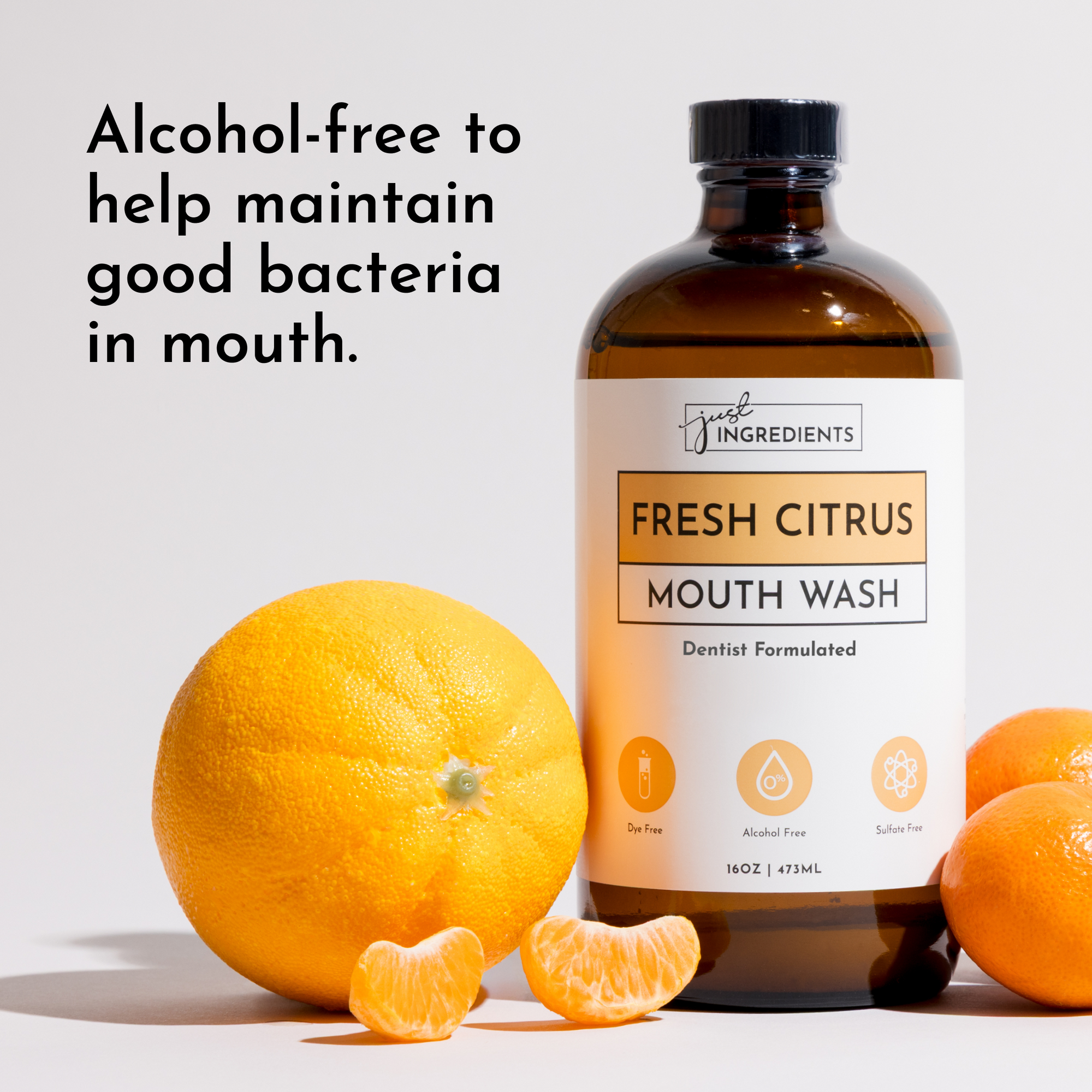 Brown glass bottle of Fresh Citrus mouthwash with whole and sliced oranges beside it on a light background.