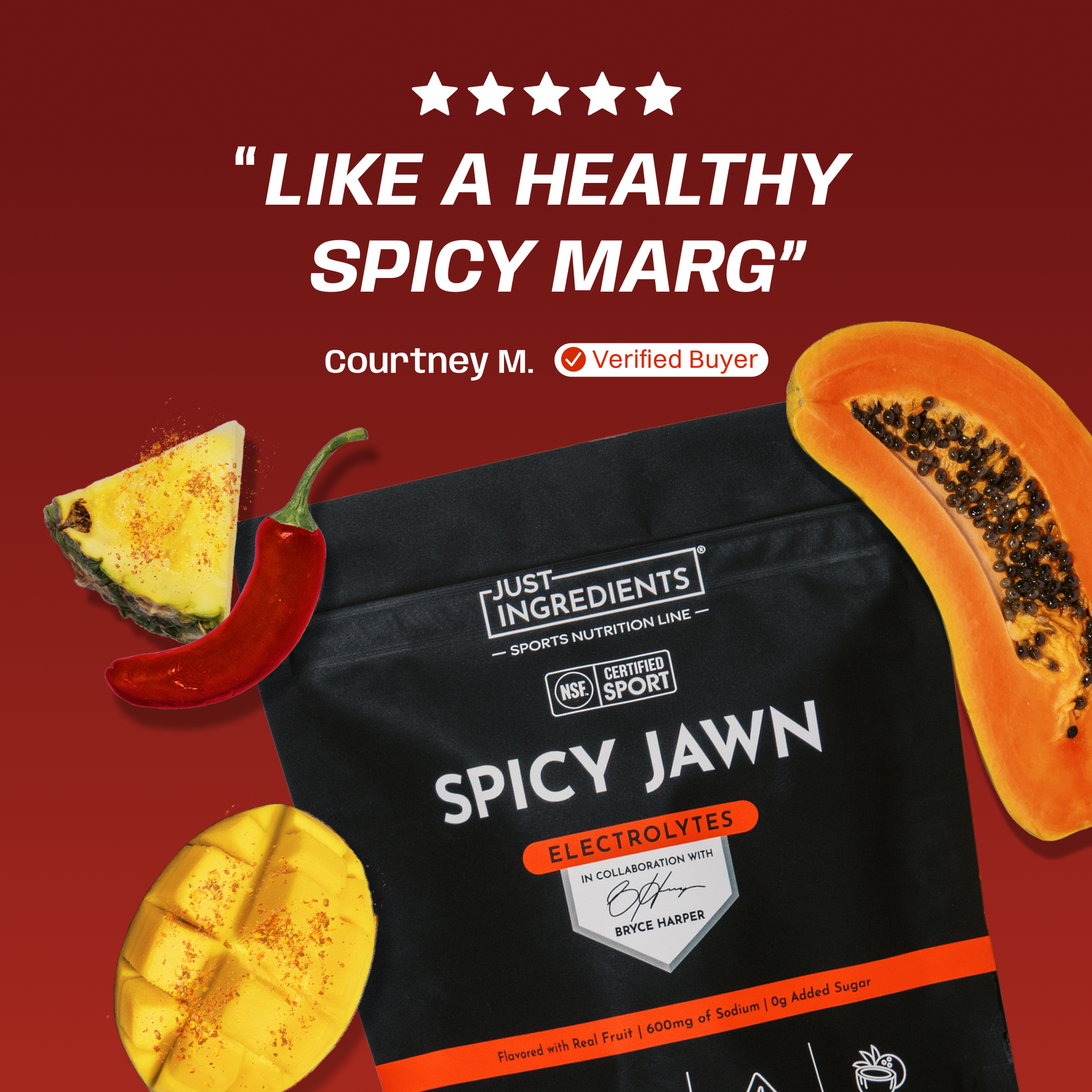 Black pouch of Spicy Jawn Electrolytes with red chili pepper, pineapple, and papaya arranged on burgundy background.