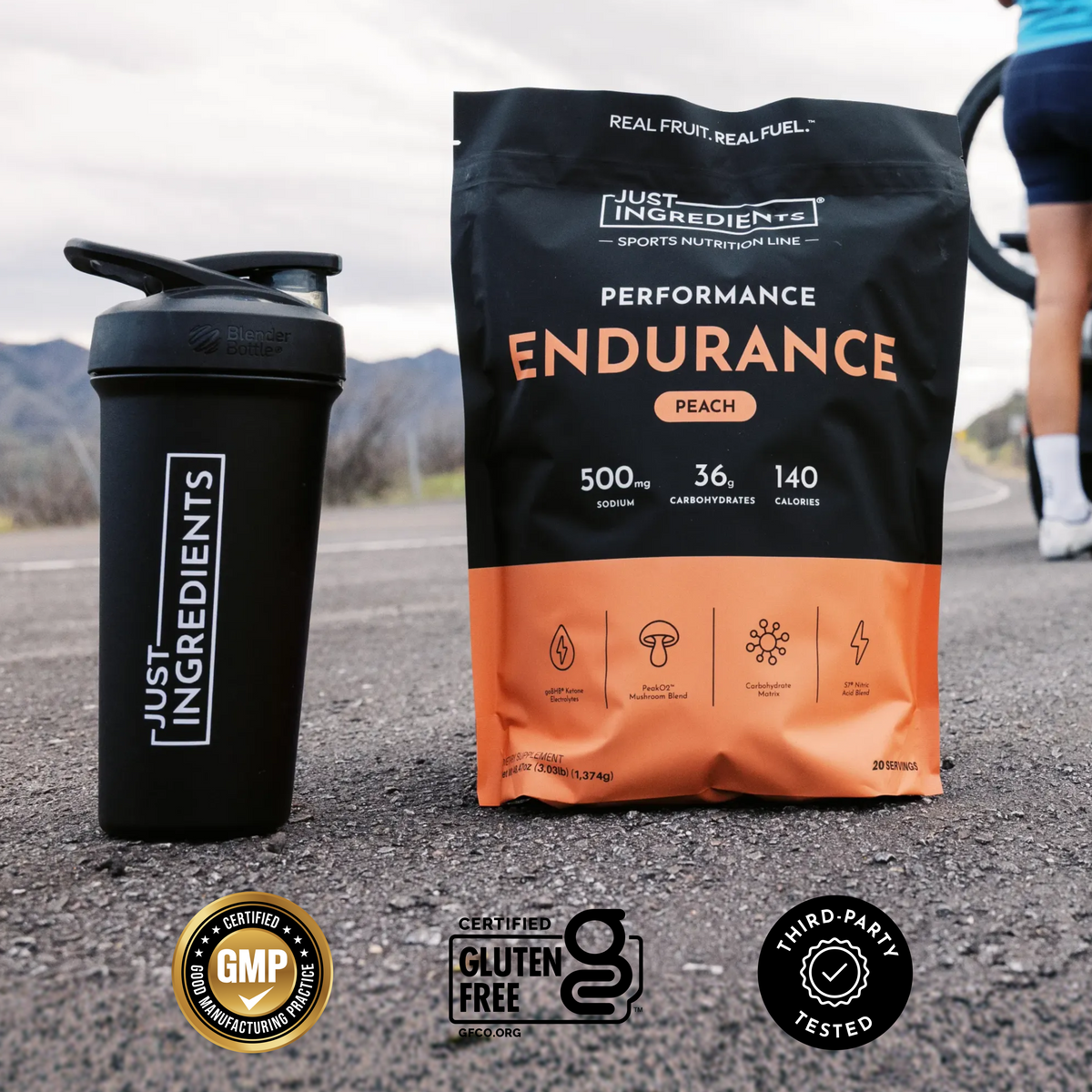 Black and orange pouch of peach endurance drink powder next to black shaker bottle on asphalt road.