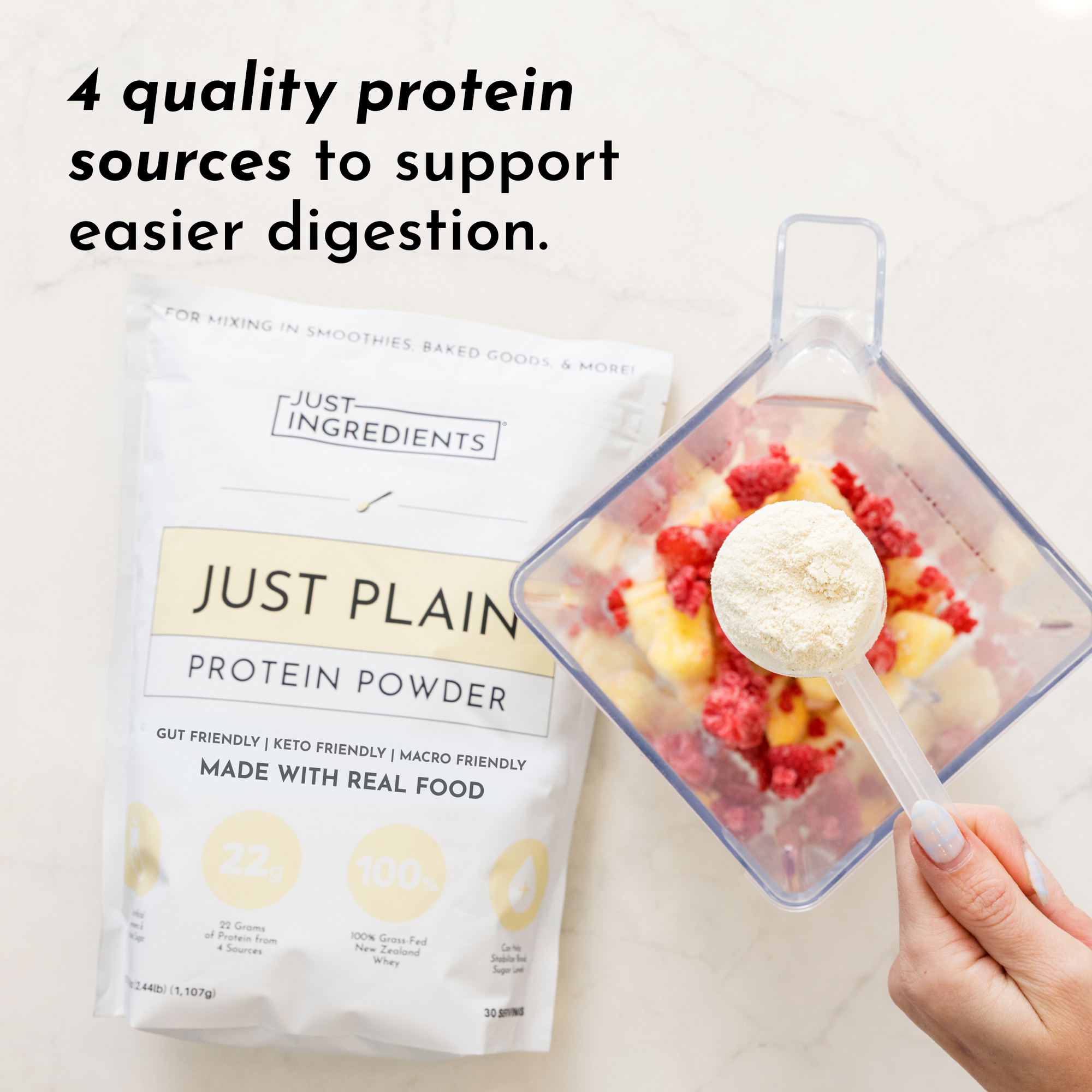 White protein powder in measuring scoop above blender with berries and fruit; product package displayed beside.