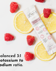 Electrolyte stick surrounded by fresh raspberries and lemon slices on a white background.