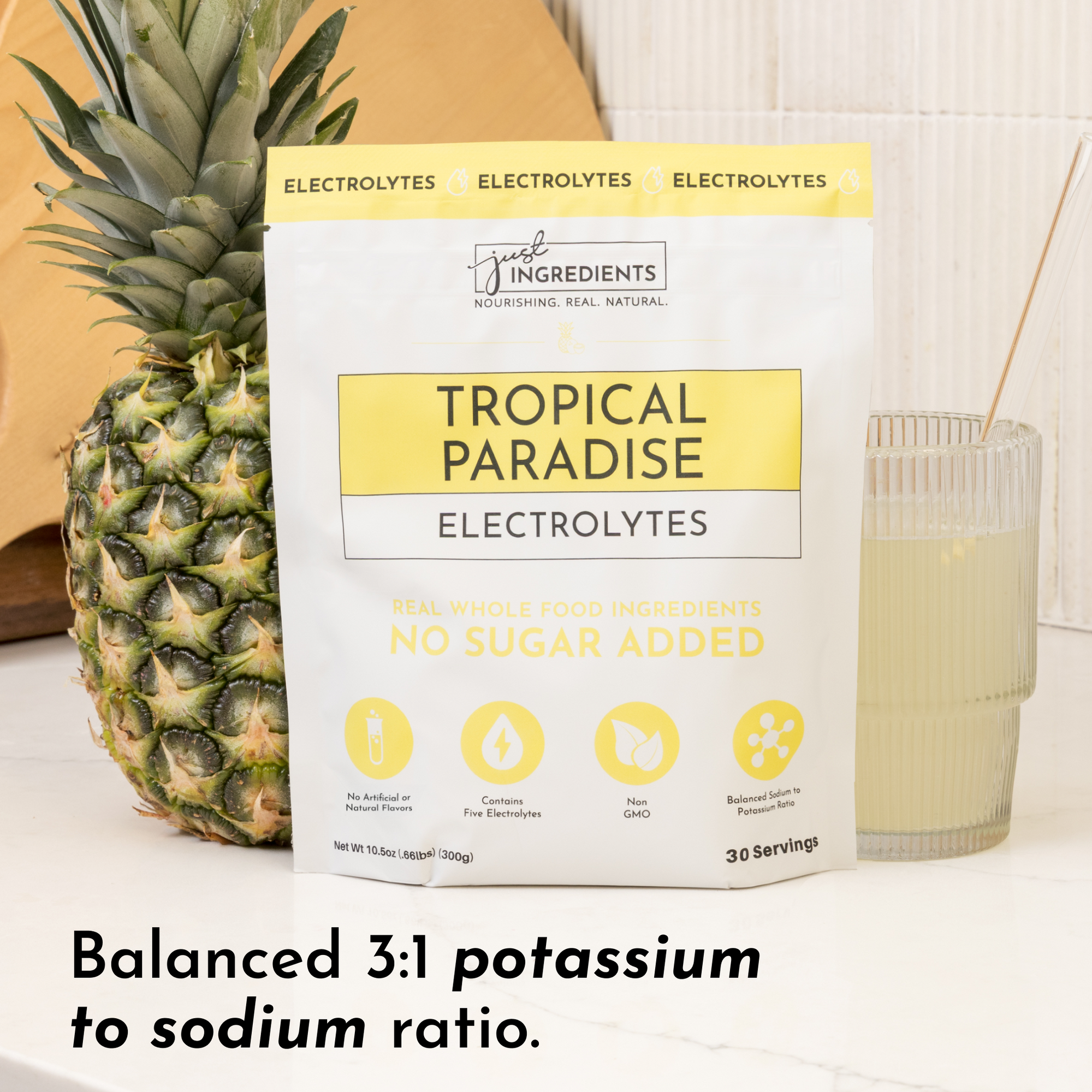 Pouch of "Tropical Paradise Electrolytes" next to a pineapple and a glass of light-colored drink on a countertop.
