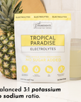 Pouch of "Tropical Paradise Electrolytes" next to a pineapple and a glass of light-colored drink on a countertop.