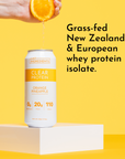 A hand squeezes an orange above a can of Clear Protein in Orange Pineapple flavor on a yellow background.