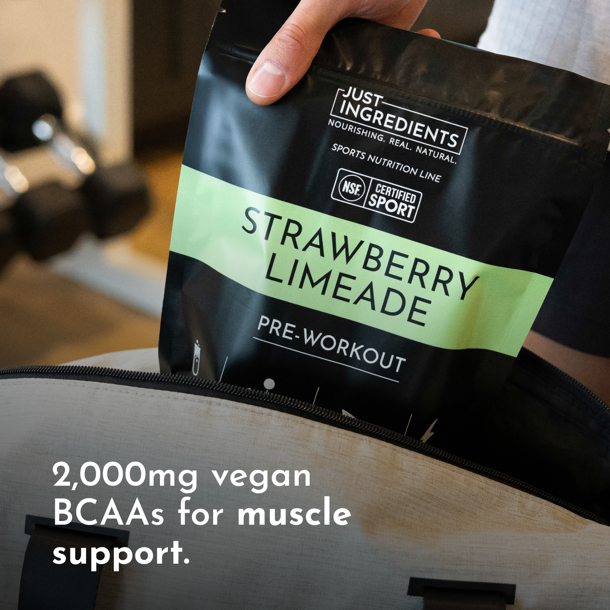 Black pouch labeled "Strawberry Limeade Pre-Workout" with text about 2,000mg vegan BCAAs, held above a gym bag.