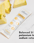 Stick packet labeled "Orange Pineapple Pre-Workout" beside fresh pineapple slices on a marble surface.